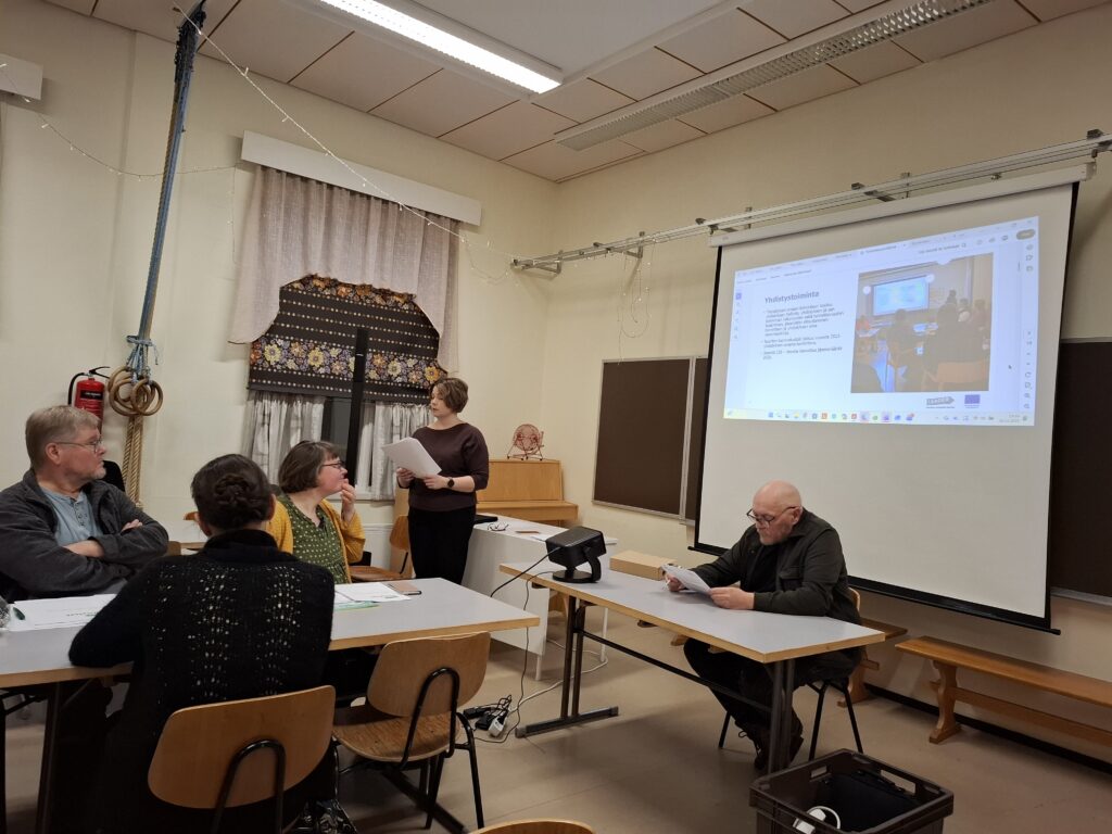 Kuva kokouspaikalta; etualalla toiminnanjohtaja Krista Järvelä esittelee toimintasuunnitelmaa, kokouksen puheenjohtajana toimiva Matti Mustajärvi istuu pöydän takana.