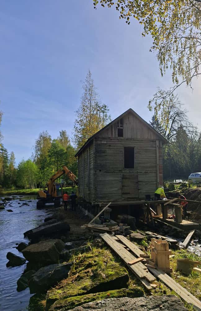 Kuvassa on mylly ja talkoolaisia vanhan myllyraknnuksen perustuksia korjaamassa. Myös kaivinkone on joessa työskentelemässä myllyn perustusten eteen.